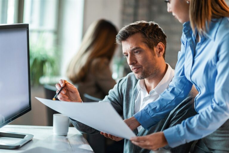Two colleagues reviewing a document and financial dashboard together at a desk